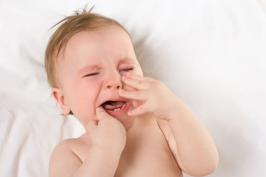 Young baby with first two teeth crying, possibly from teething pain. 